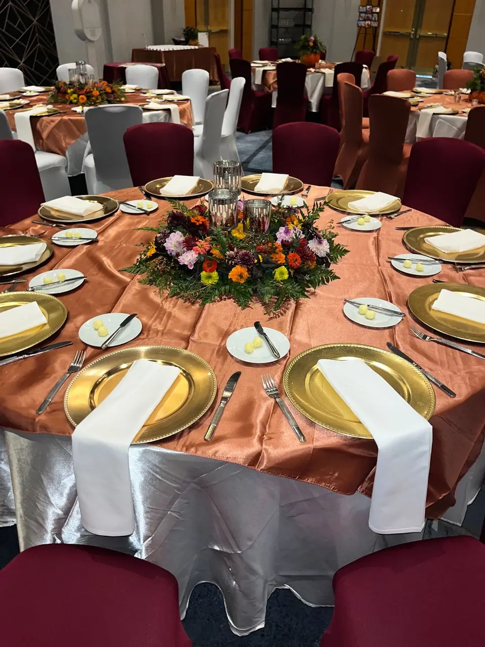 Round banquet table with gold chargers, white napkins and a colorful floral centerpiece