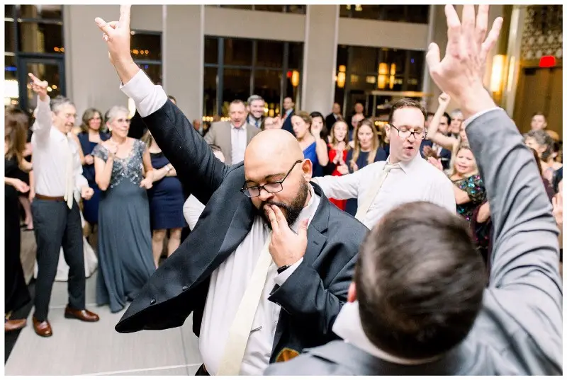 Guest in glasses points up and dances with other guests with arms raised
