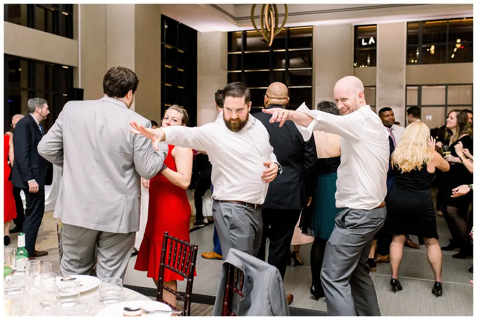 Wedding guests dance and reach out their arms on a ballroom dance floor