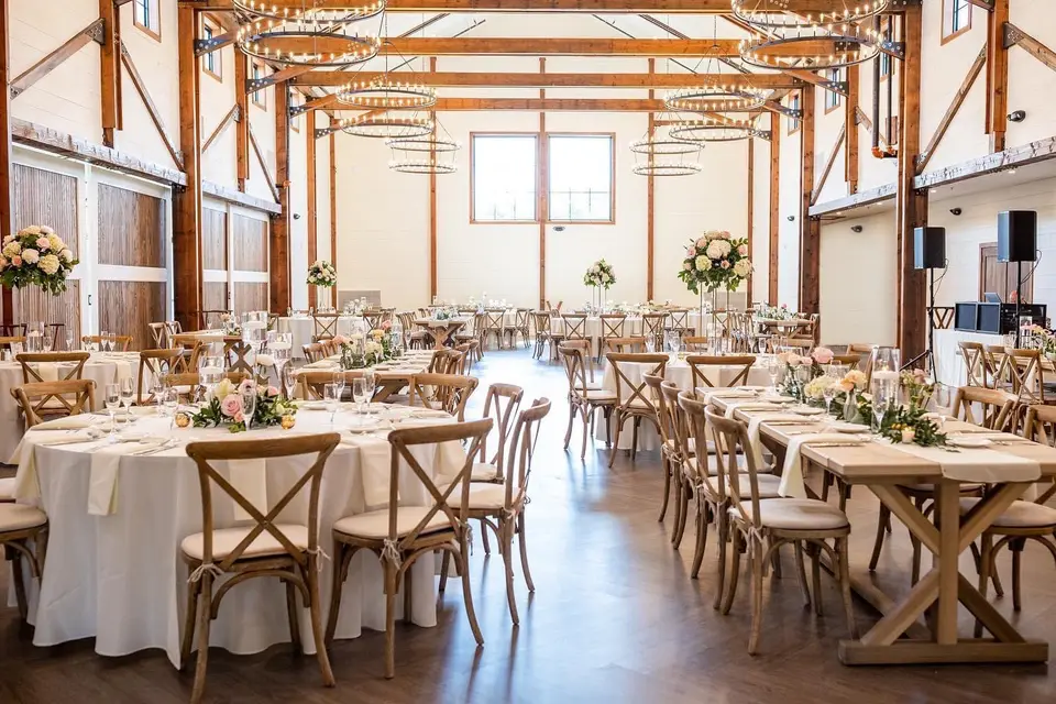 Barn reception room with white-linen and wooden farm tables, cross-back chairs and a chandelier