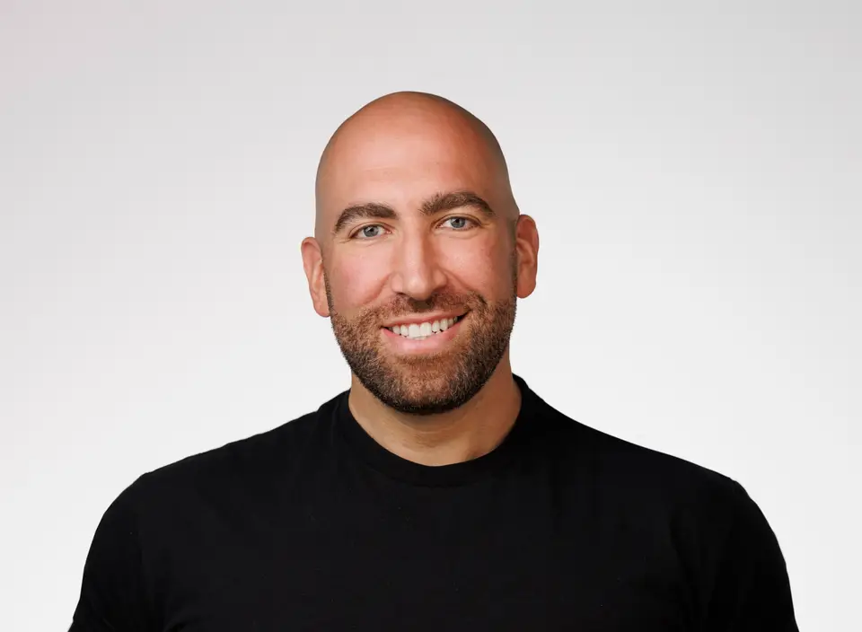 Smiling bald bearded man in a black shirt against a plain gray background