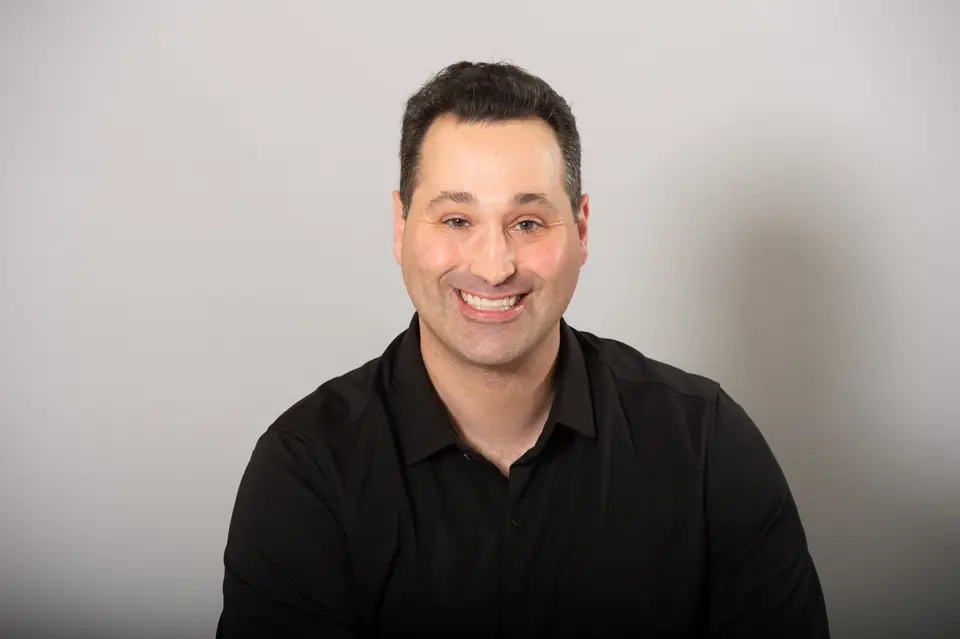 Smiling man with short dark hair in a black shirt against a gray background