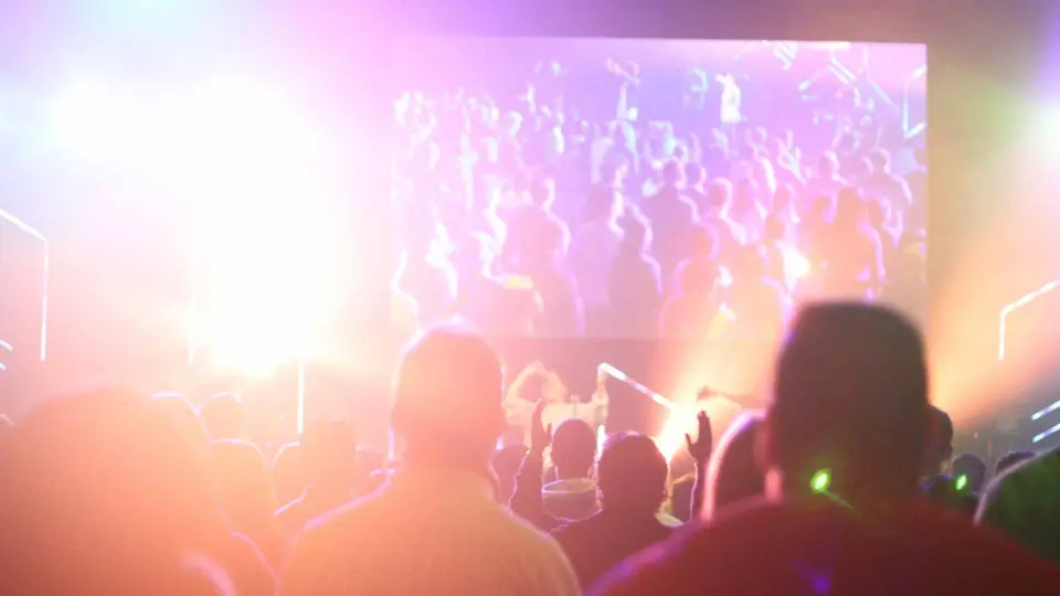 Crowd seen from behind watching a large video screen with bright stage lights